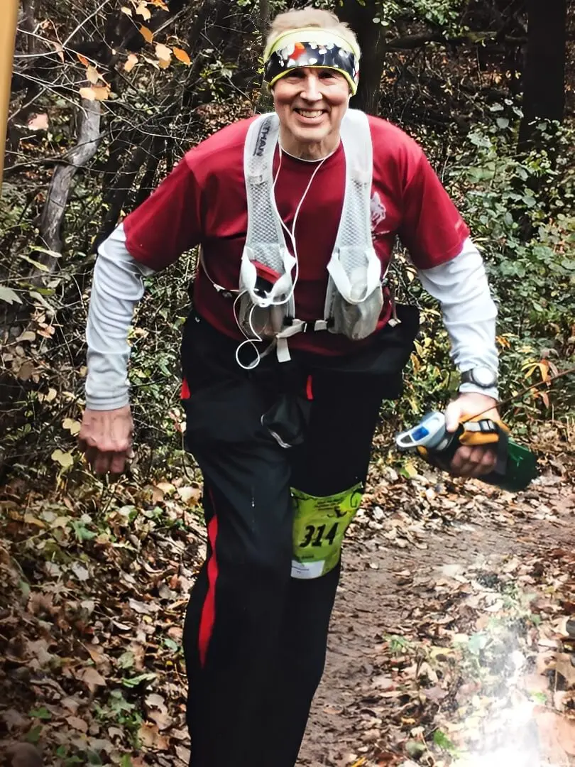 Runner on forest trail with hydration gear.